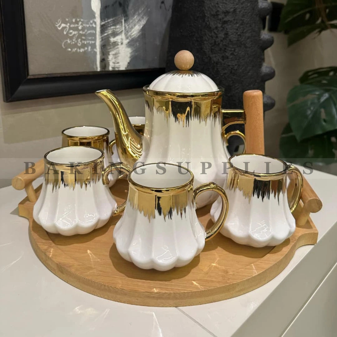 Ceramic tea set with gold accents on a wooden tray, featuring a teapot and six cups.