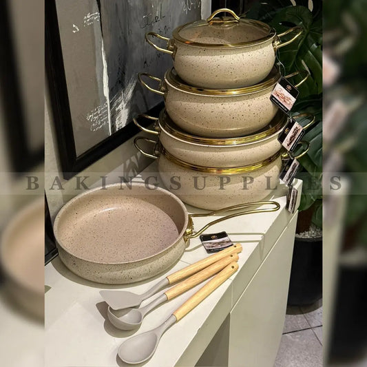Set of ceramic cookware with gold accents on a display stand, accompanied by wooden utensils.