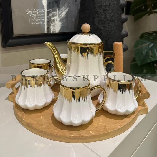 Ceramic tea set with gold accents on a wooden tray, featuring a teapot and six  cups.