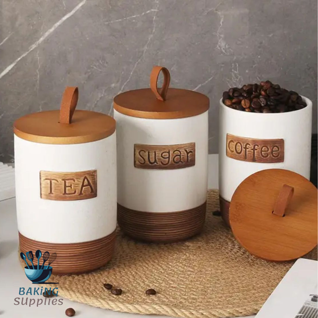 Set of ceramic kitchen canisters labeled 'Tea', 'Sugar', and 'Coffee' on a marble surface.